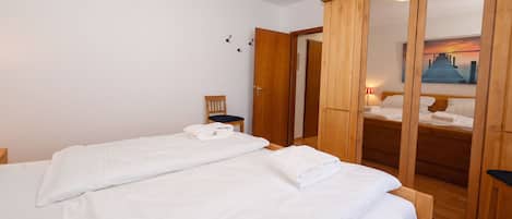 A bedroom with two beds, wooden wardrobe, and a view of a pier through a mirror.