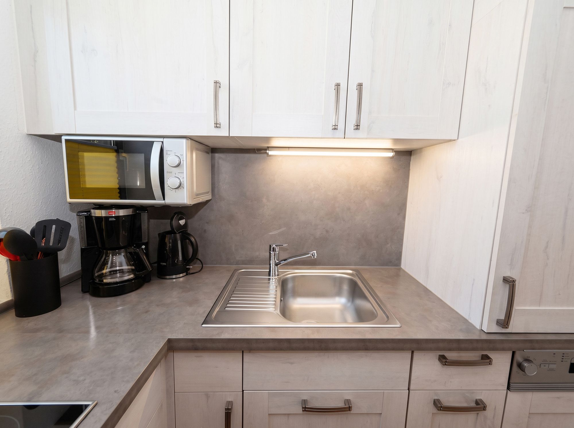 Een moderne keuken met een ingebouwde magnetron, koffiezetapparaat en een roestvrijstalen spoelbak.