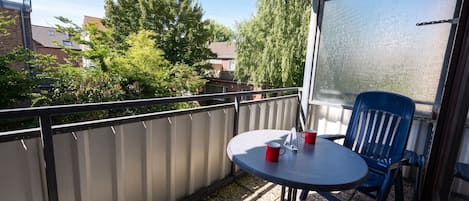 A balcony with a table and chairs, a red mug, and a view of trees and buildings.