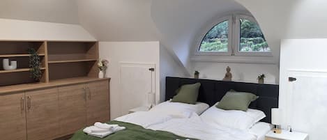 Une chambre à coucher comprenant un lit, une table de chevet, une armoire et une fenêtre donnant sur un paysage verdoyant.