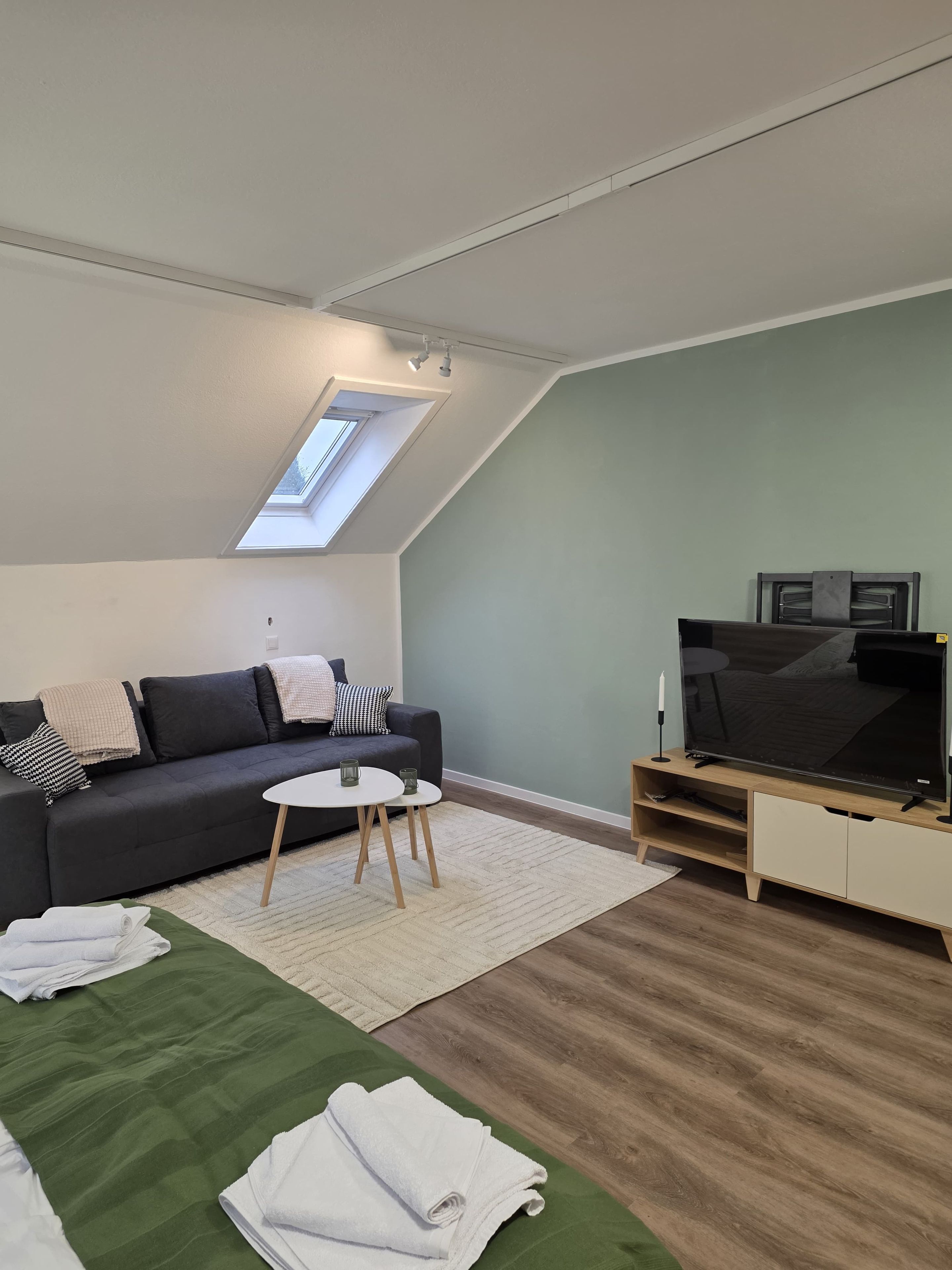 Ein modernes Wohnzimmer mit schrägverdachter Decke, einer Couch, einem Fernsehschrank und einem kleinen Tisch.