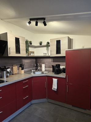A modern kitchen with red cabinets, a stainless steel sink, and a coffee maker.
