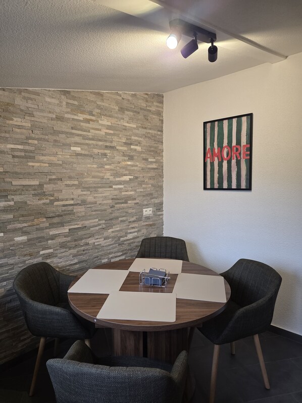 A conference room with a round table, four chairs, a wall-mounted projector, and a 'AMORE' framed artwork.