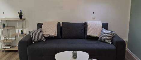 A modern living room with a dark grey sofa, two white coffee tables, a small potted plant, and a skylight above.