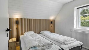 Ein Schlafzimmer mit zwei Einzelbetten, einer Wand aus Holzlatten, einem Fenster und einer Heizung.