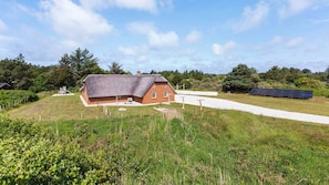A thatched-roof house with a gravel path leading to it, surrounded by greenery and a solar panel array. - VillaVilla 1005 - Vester Husby, Vestjylland (Ulfborg)