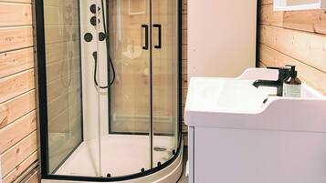 A wooden interior with a glass-enclosed shower, a white sink, and a toilet.