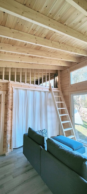 A room with a wooden ceiling, a staircase, a window, and a sofa.