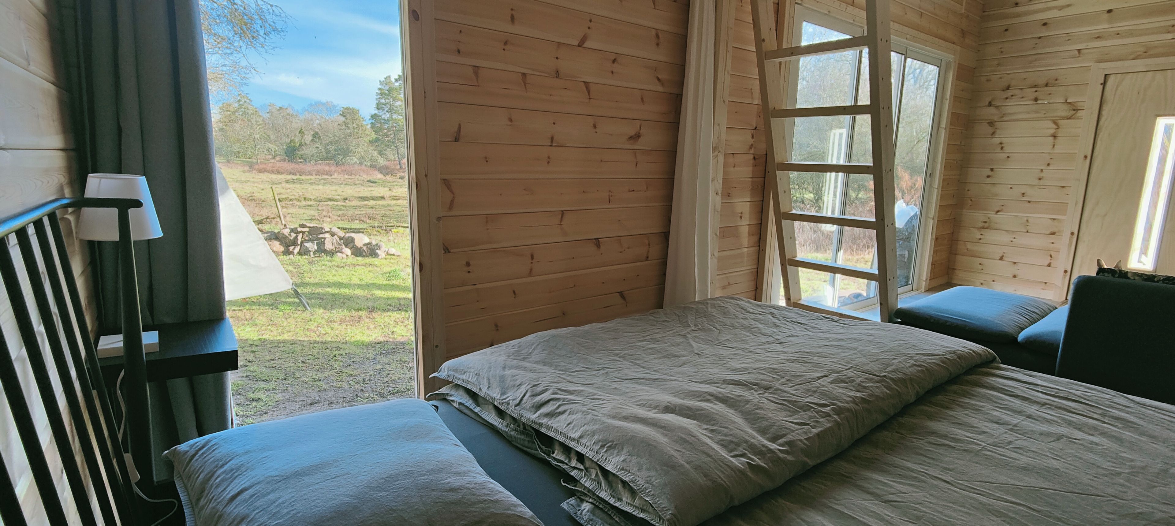 A wooden cabin room with a bed, a window, and a view of a grassy field.