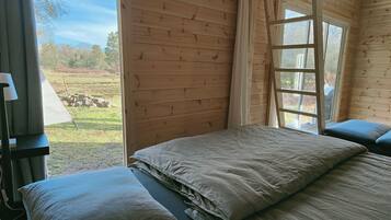 A wooden cabin room with a bed, a window, and a view of a grassy field.