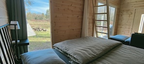 A wooden cabin room with a bed, a window, and a view of a grassy field.