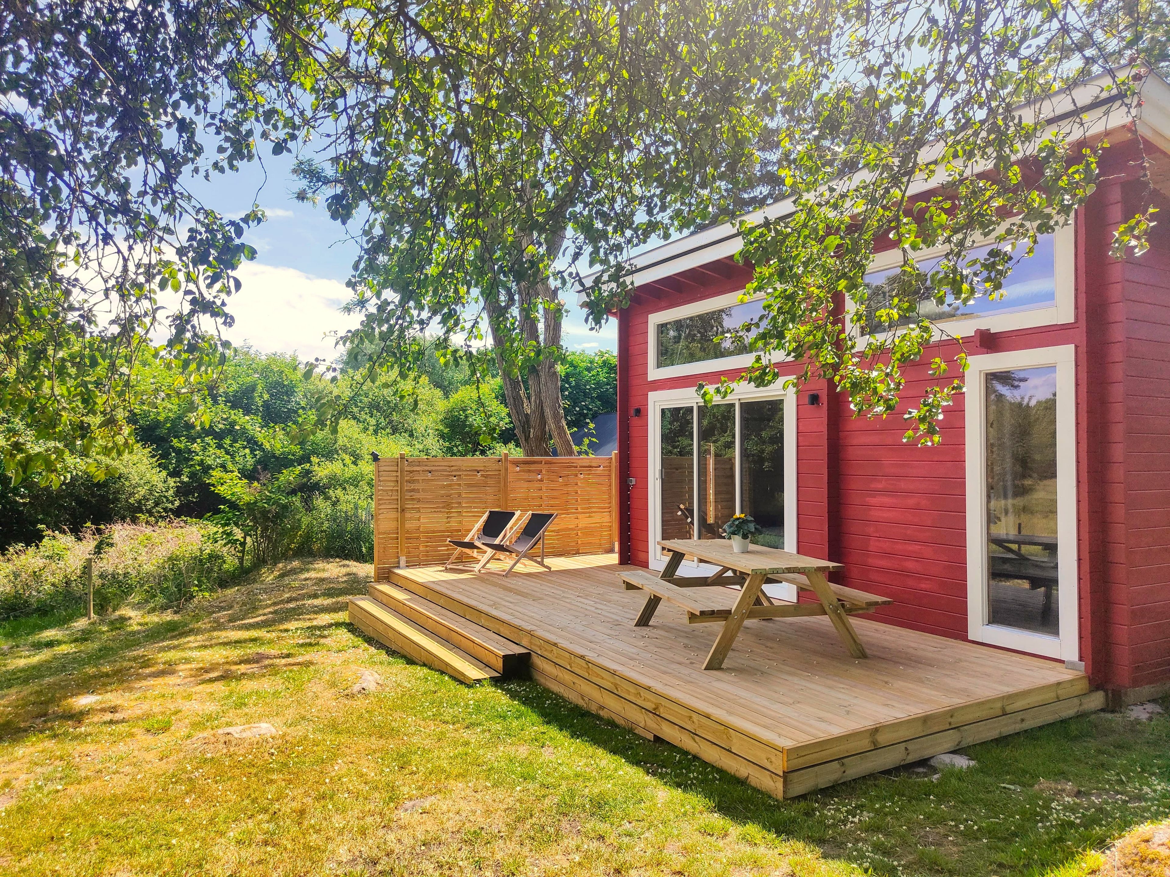 A red building with a wooden deck, two lounge chairs, and a picnic table.