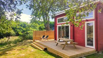 A red building with a wooden deck, two lounge chairs, and a picnic table.