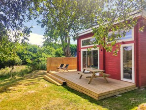A red building with a wooden deck, two lounge chairs, and a picnic table.