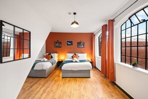 Quarto moderno com duas camas, teto inclinado e janelas amplas.
