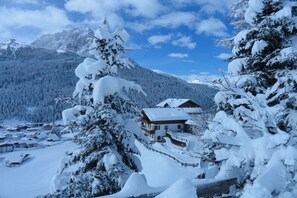 A snow-covered mountain landscape with a house surrounded by trees.