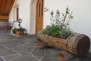 A rustic outdoor area with a stone floor, wooden barrel planter with greenery, and a wooden door.
