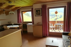 A cozy room with a dining area, a kitchen, and a balcony with a view of the countryside.