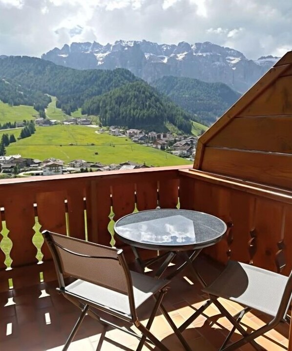 Un balcon avec une table ronde et deux chaises, donnant sur un paysage montagneux avec un village en contrebas.