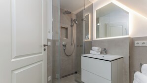 Un baño moderno con ducha envuelta en cristal, tocador blanco con espejo y un perchero para toallas.