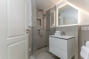 Casa de banho moderna com chuveiro em cabine de vidro, toucador branco com espelho e porta-toalhas.