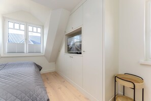 A bedroom with a bed, a window, a wardrobe, and a small stool. - Your modern North Sea getaway on Sylt for a relaxing vacation by the coast (Sylt)