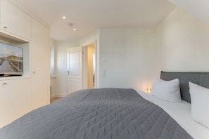 Quarto com cama, televisão presa a um móvel e porta que dá para outro cômodo.