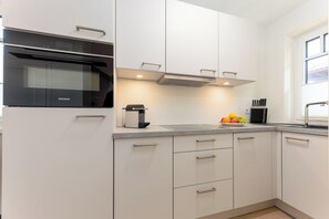A modern kitchen with white cabinetry, a black oven, and a stainless steel range hood. - Your modern North Sea getaway on Sylt for a relaxing vacation by the coast (Sylt)