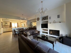 A modern living room with a sofa, dining table, and a fireplace. - Psichro Apartments Hera 1st Floor (Lasithi Plateau)