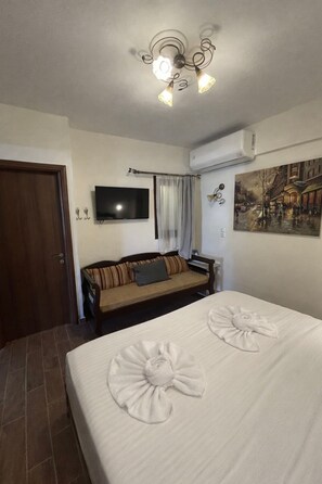 Ein Hotelzimmer mit Bett, Sofa, Fernseher, einem Gemälde und einer Deckenleuchte.