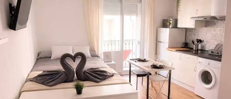 A modern hotel room with a bed, a desk, a washing machine, and a balcony.