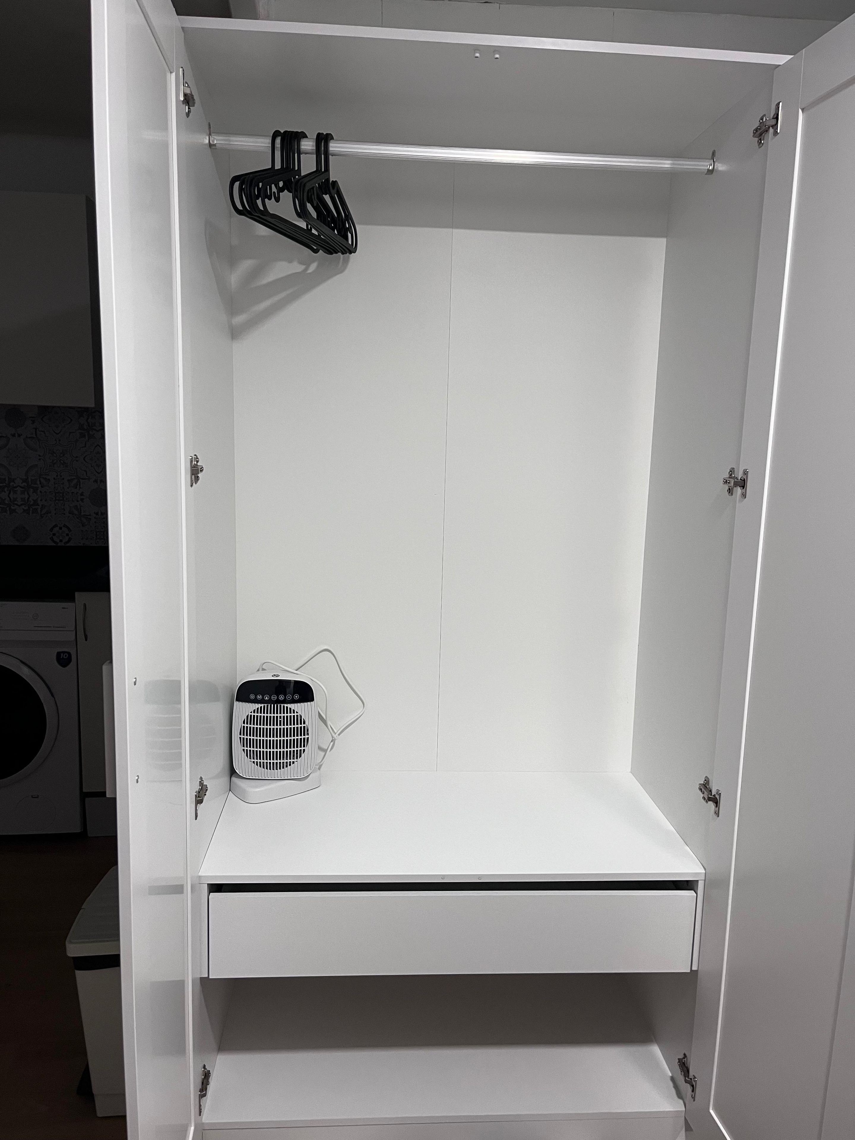 A white wardrobe with a hanging rack, a fan, and a built-in washing machine.