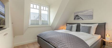 A bedroom with a bed, a window, a painting, and a nightstand with a lamp.
