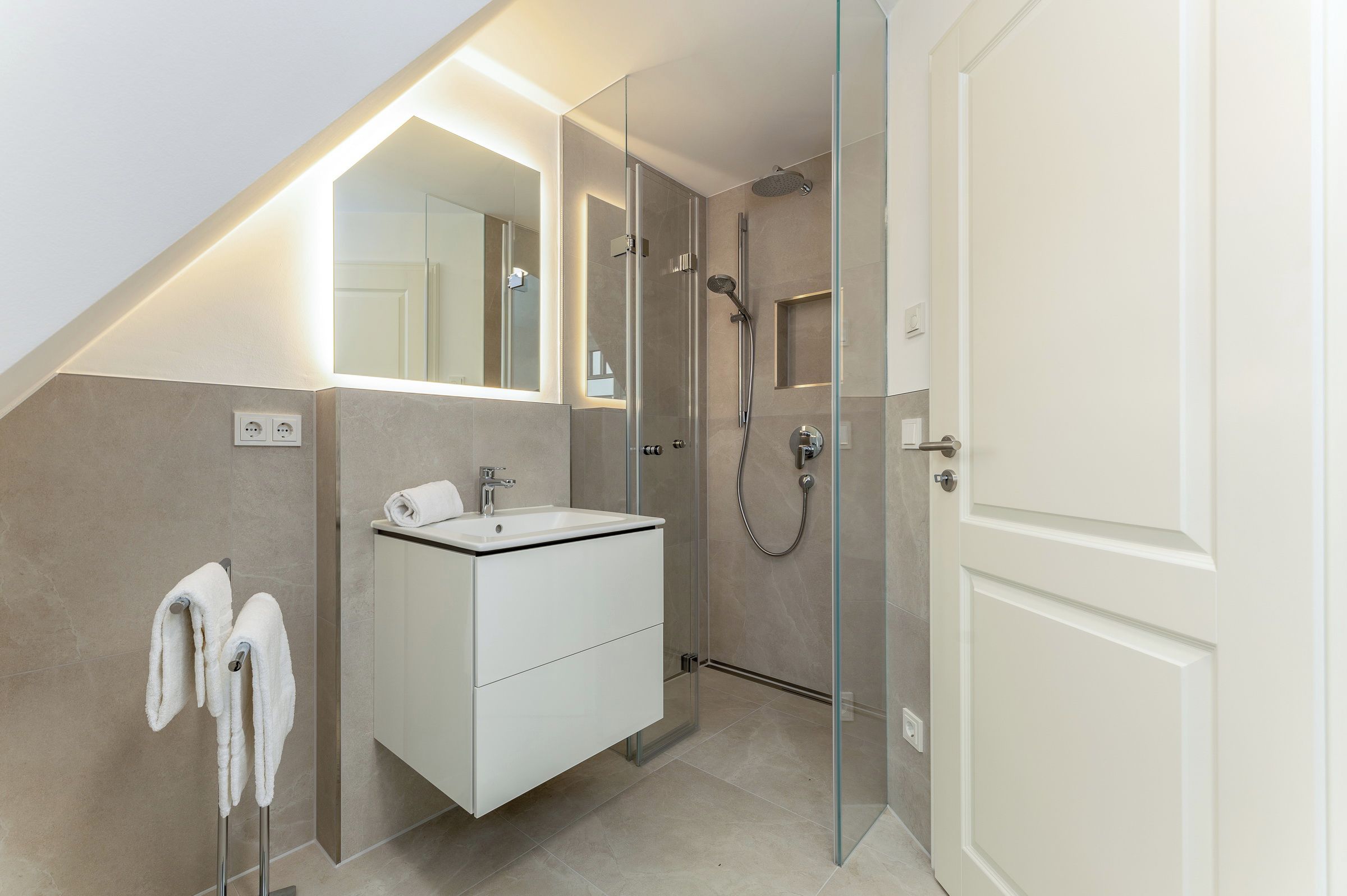 Un baño moderno con cabina de ducha de vidrio, un tocador blanco y un espejo grande.