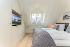 A bedroom with a bed, a TV mounted on a wall, a window with blinds, and a painting on the wall. - Exclusive vacation rental on Sylt with a terrace and modern amenities (Sylt)