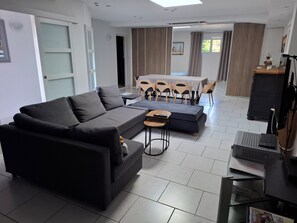 A modern living room with a dark grey sofa, a small coffee table, and a dining area with a table and chairs. - Lovely apartment in a quiet neighborhood perfect for your stay (SECLIN)