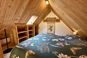 A bedroom with a sloped ceiling, wooden beams, a skylight, a bed with a floral bedspread, a wooden wardrobe, and a framed picture on the wall. - Holiday home in Limmen with swimming pool (Limmen)