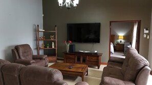 A living room with leather sofas, a wooden coffee table, a TV, and a bookshelf with decorative items.