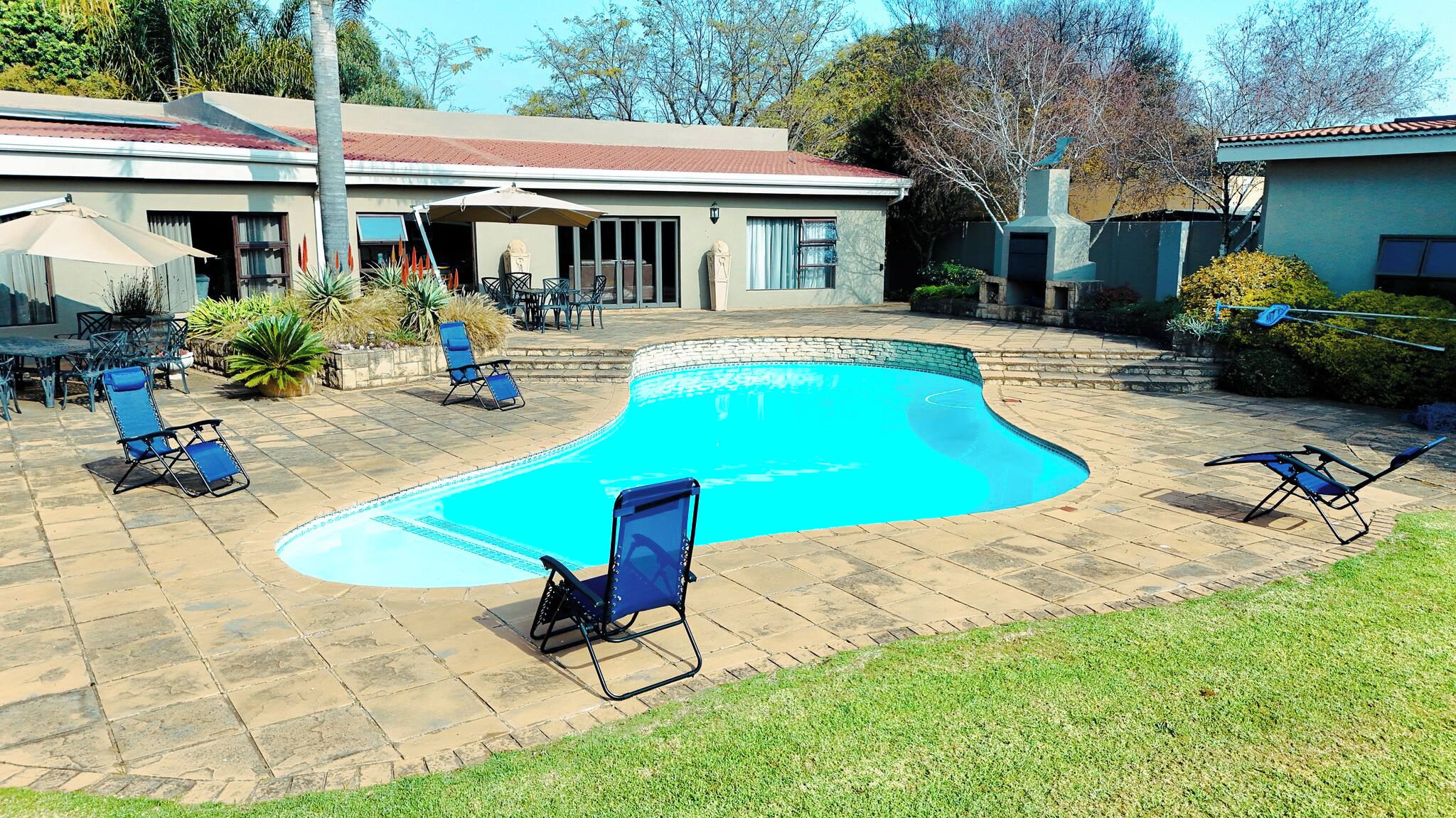 A swimming pool with lounge chairs, a patio area, and a house in the background.