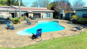 A swimming pool with lounge chairs, a patio area, and a house in the background.