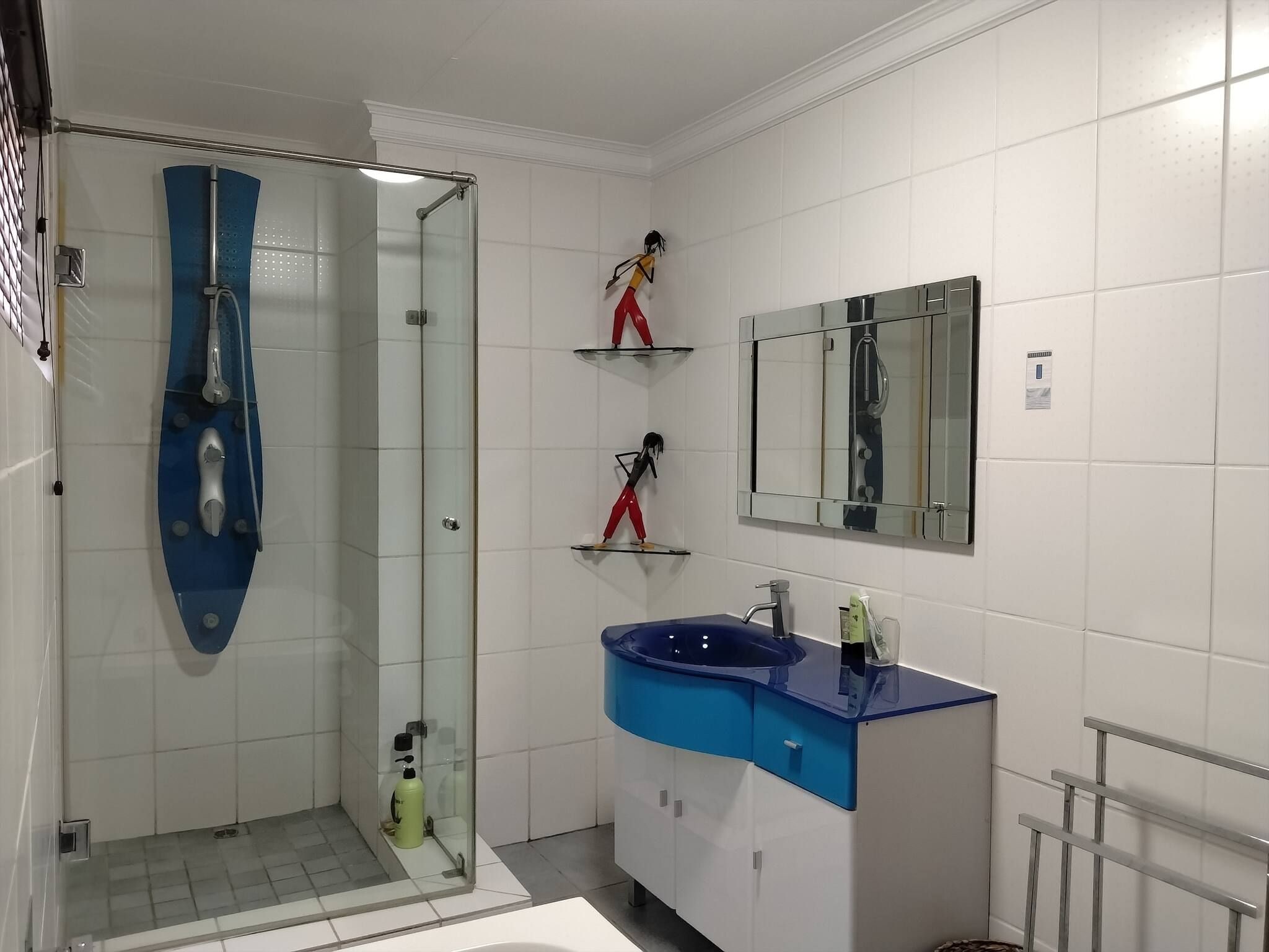A modern bathroom with a glass-enclosed shower, a blue sink, and a mirror above the vanity.