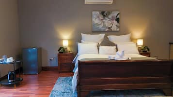 Una habitación de hotel con una cama de madera, mesitas de noche con lámparas, un escritorio pequeño con una computadora, una cafetera y un cuadro en la pared.
