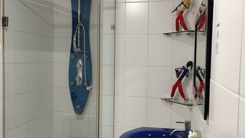A bathroom with a glass-enclosed shower, a blue bathtub, and a mirror with decorative figures.