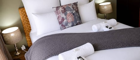 Une chambre d’hôtel avec un lit bien fait, un coussin décoratif, une couverture grise et un ensemble de produits de toilette posés sur le lit.