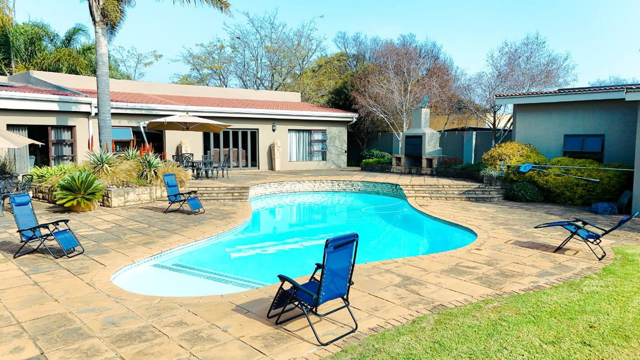 A swimming pool with lounge chairs, a covered patio, and a house with a red roof.