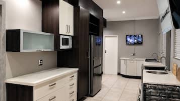 Una cocina moderna con microondas integrado, refrigerador, estufa y televisor montado en la pared.