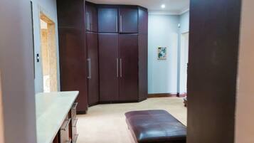 Quarto com cozinha compacta, guarda-roupa de madeira escura e um pequeno banco.