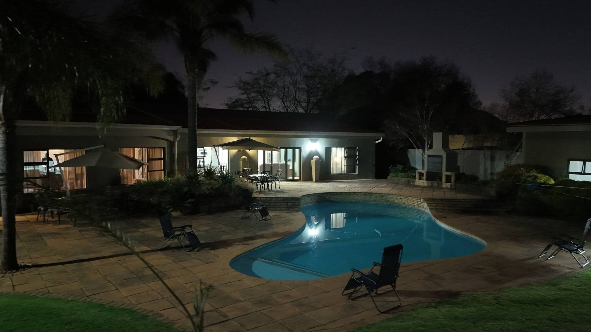 Una piscina de borde curvo, rodeada por una zona de patio con sillas y una mesa.