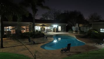 Una piscina de borde curvo, rodeada por una zona de patio con sillas y una mesa.