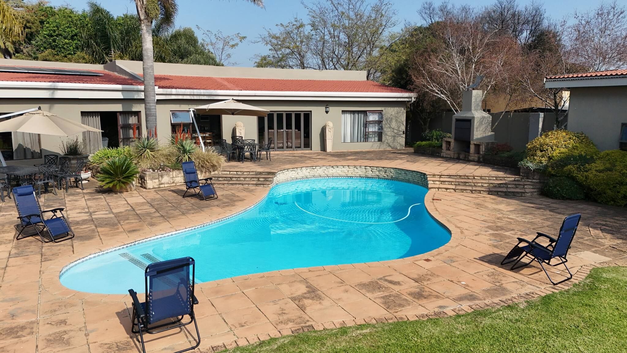 A swimming pool with a curved edge, surrounded by a patio with lounge chairs and a covered outdoor seating area.